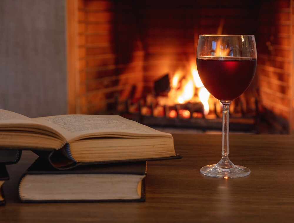 A glass of wine sits on a table beside books.